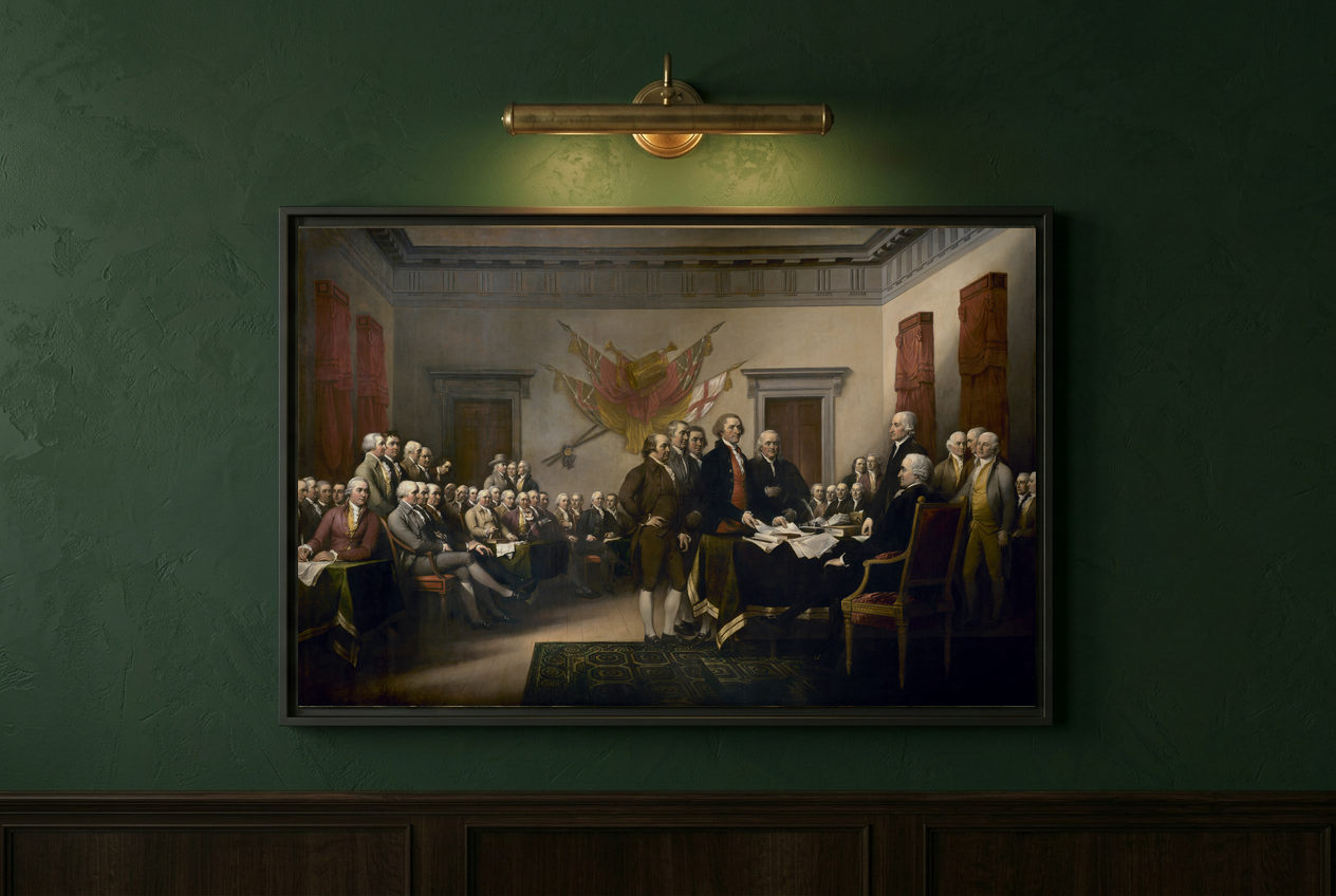Close-up of the Declaration of Independence framed canvas on a deep sage green wall lit by a brass picture light
